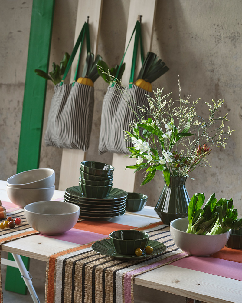 A wooden table in an industrial-style room is set with various table essentials from the MÄVINN collection.