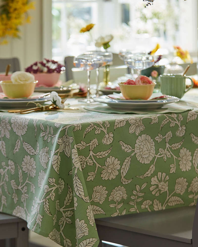 A festive spring table, set with a green SMÖRFISK tablecloth, yellow UPPLAGA bowls and green and pink SMÖRFISK mugs