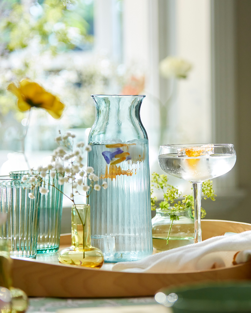 A light turquoise SMÖRFISK carafe surrounded by decorative vases and elegant glassware on a table.