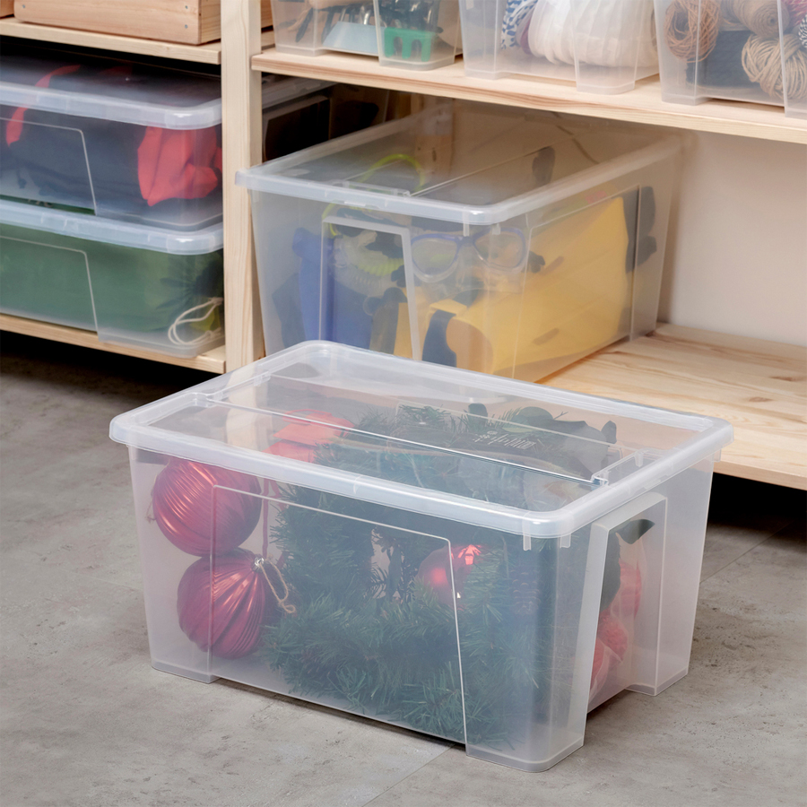 Clear plastic storage box with lid containing Christmas decorations, placed in front of a wooden shelving unit with additional storage boxes.