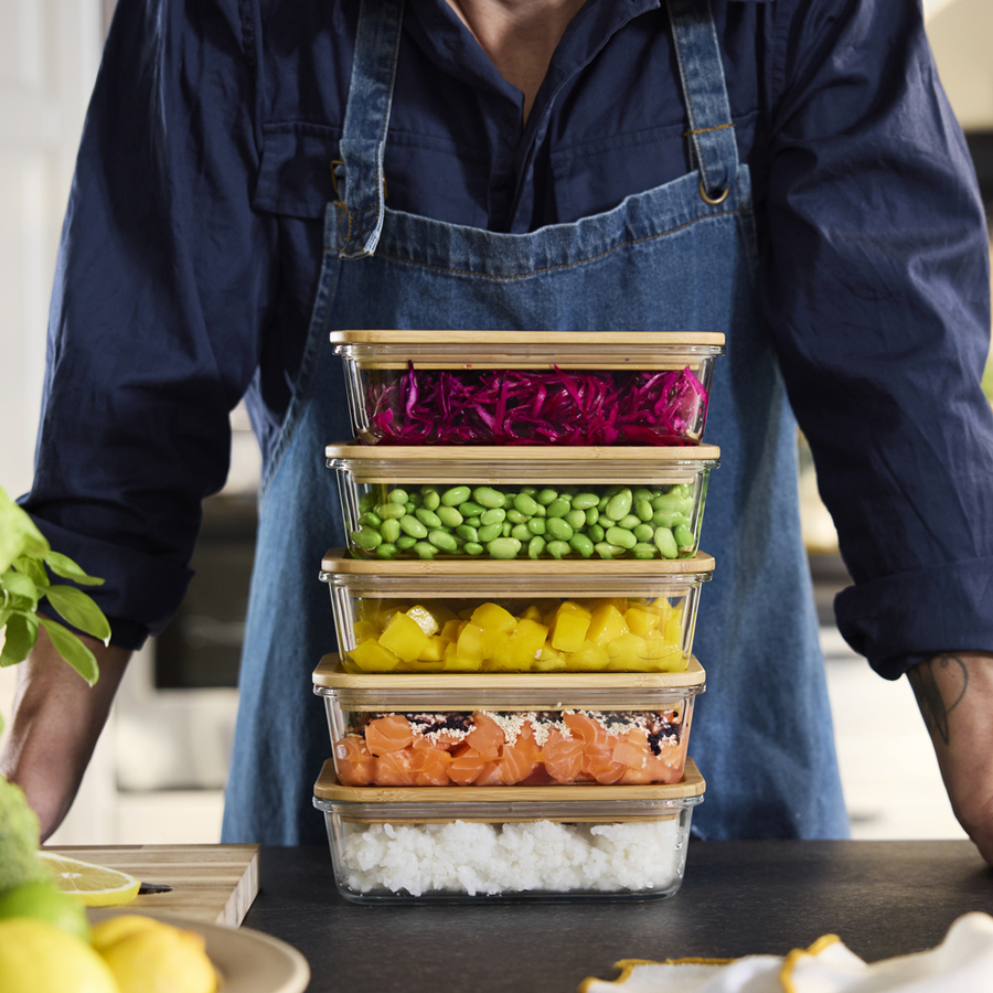 Stacked glass food containers with wooden lids holding colorful prepared ingredients.