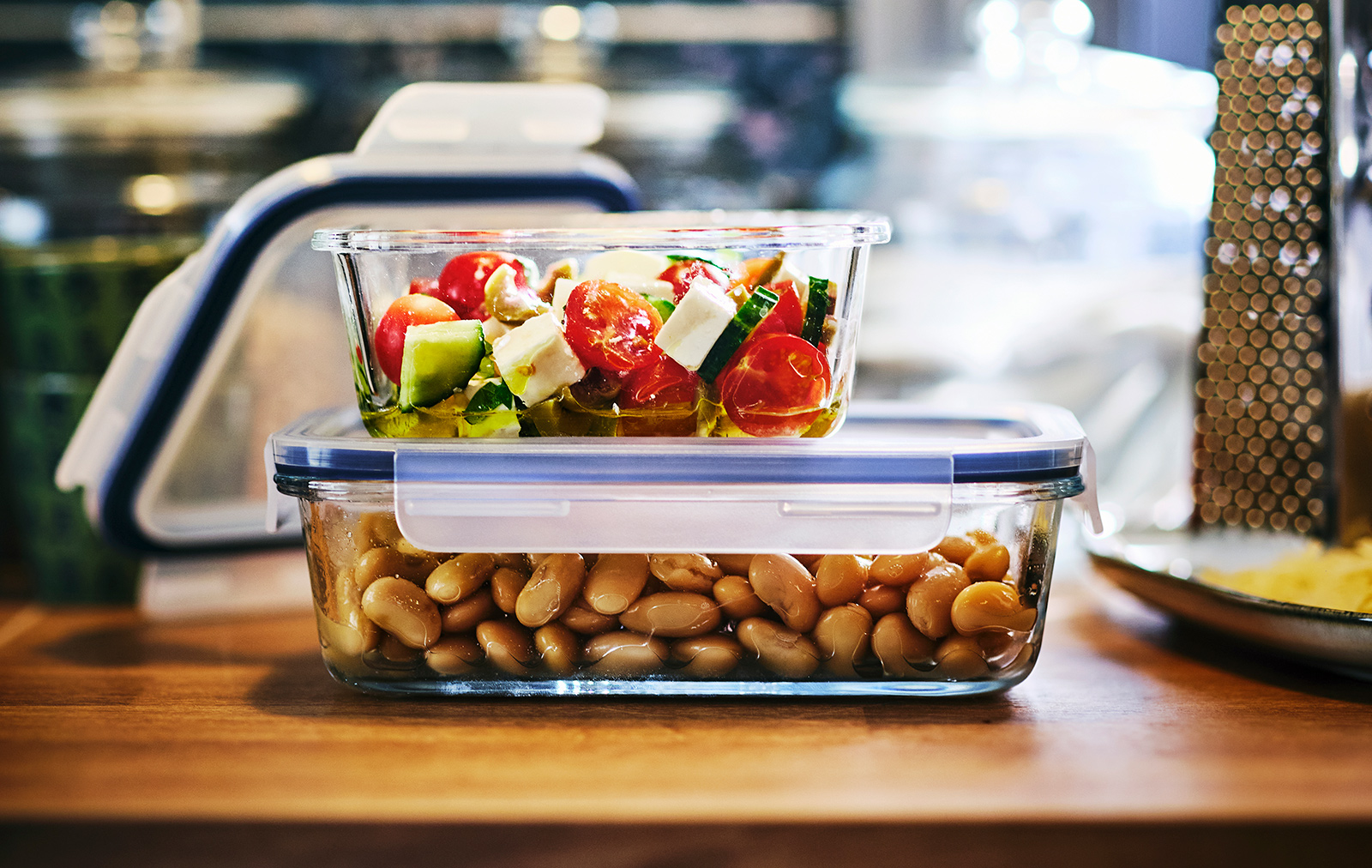 A small IKEA 365+ glass food container filled with a salad is on top of a larger IKEA 365+ container filled with beans.