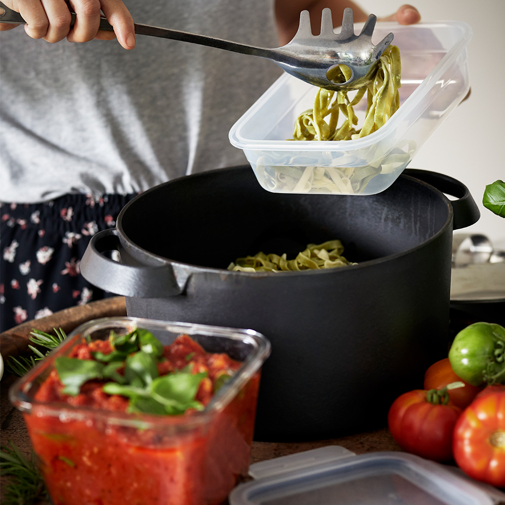 A kitchen setting shows a person using IKEA 365+ food containers to store freshly cooked pasta and tomato sauce.