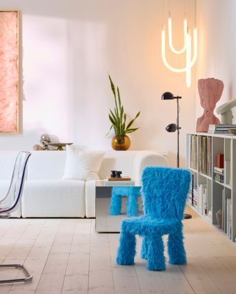 Una silla infantil con una funda GRESIMOJS de piel sintética azul en una sala de estar luminosa y moderna, junto a una mesita auxiliar con espejo.