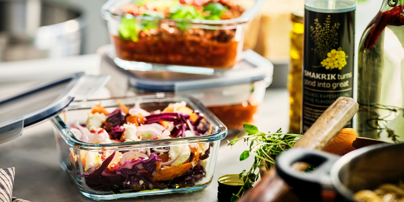 A IKEA 365+ glass food storage container with prepared food is next to a pan. Two other containers are stacked behind it.