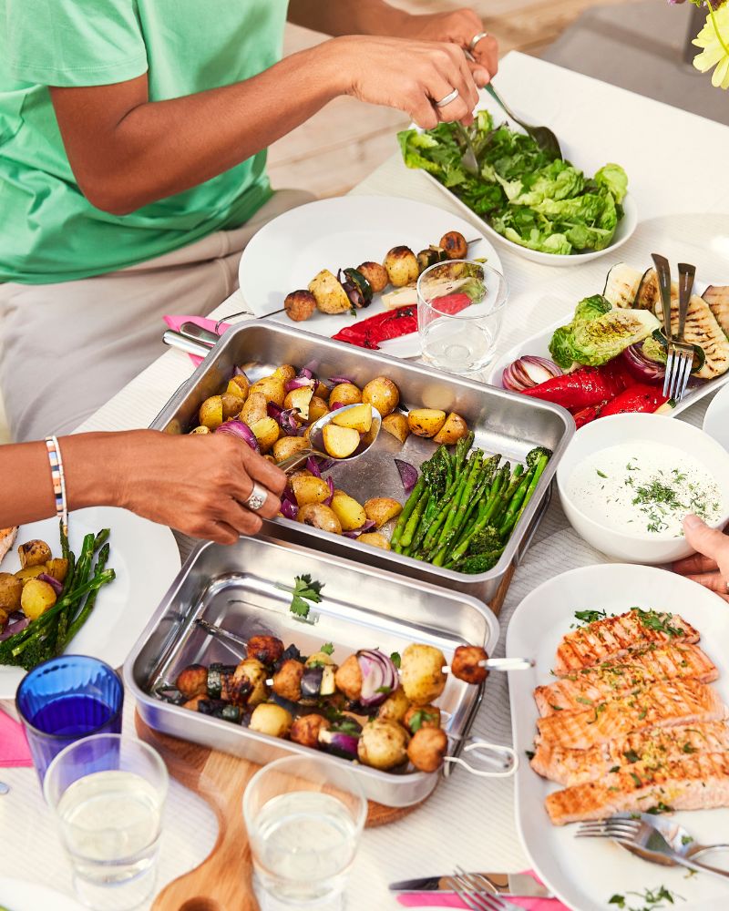 A group of people serve themselves SJÖRAPPORT salmon fillets, roasted potatoes and vegetables from IKEA 365+ serving plates.
