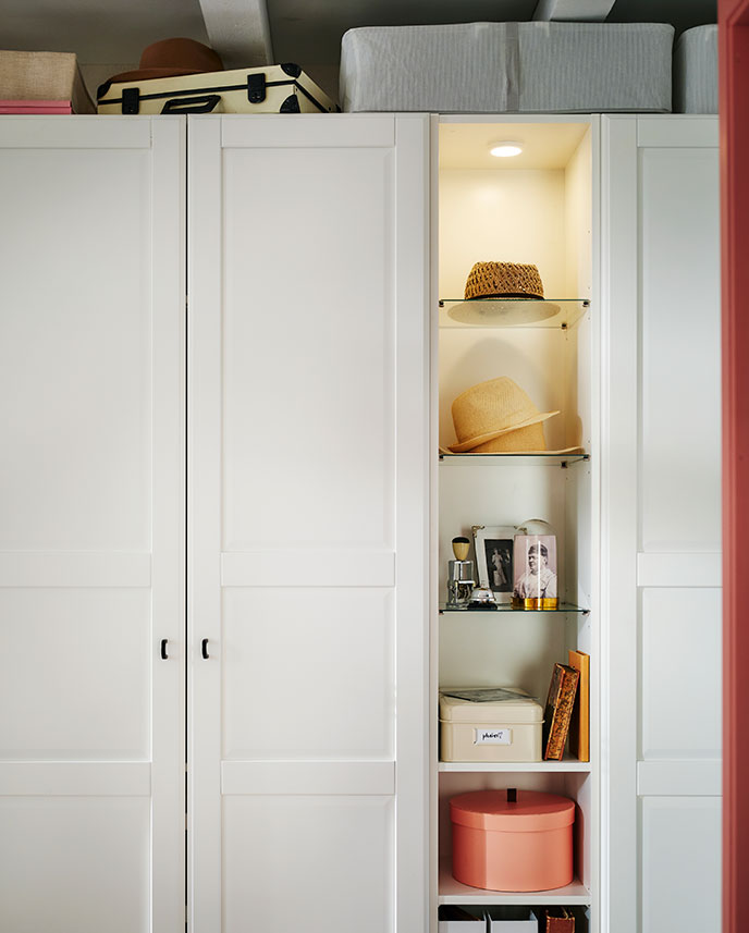 A white PAX/TYSSEDAL wardrobe with mid-unit has hats, knick-knacks and boxes on the shelves and larger storage boxes on top.