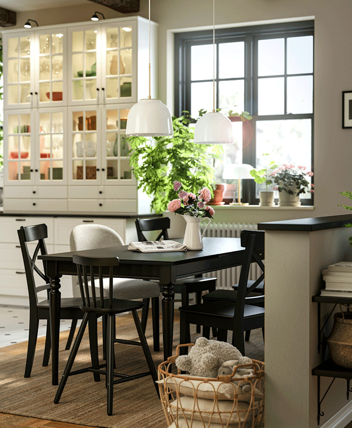 Black wooden dining table with matching chairs and a grey upholstered chair on a jute rug. White pendant lamps hang above, with a glass-door cabinet in the background.