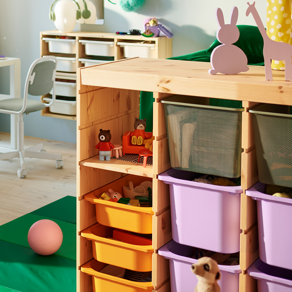 Dos separadores de ambiente TROFAST de pino blanqueado claro que contienen una mezcla de cajas de colores en medio de un dormitorio infantil.