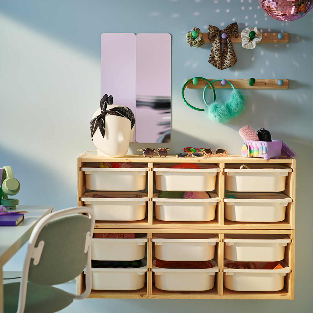 Dos estructuras de almacenamiento de pared TROFAST de pino blanqueado claro en una pared, con cajas blancas en su interior. Encima hay dos percheros con pomos FLISAT.