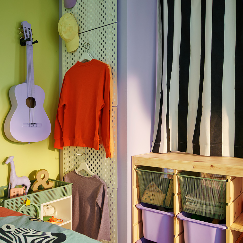 Un separador de ambiente TROFAST con una cortina de rayas blancas y negras cerrada sobre él, junto a una columna de cuatro paneles perforados SKÅDIS blancos.