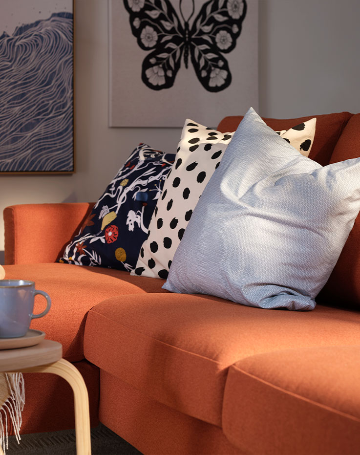 A living room with a red-brown SALTSJÖBADEN three seat sofa with chaise longue, complemented by decorative cushions.