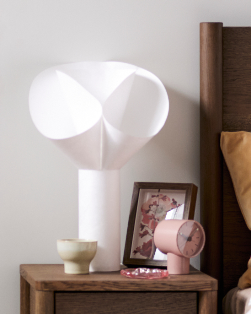 White BÄCKNATE table lamp on a bedside table with a wooden frame and table clock.