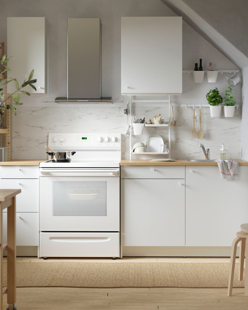 A kitchen with a new layout featuring an UNDANTAG hood, two light‑wood KYRRE stools, and an adjustable SUNNERSTA rail.