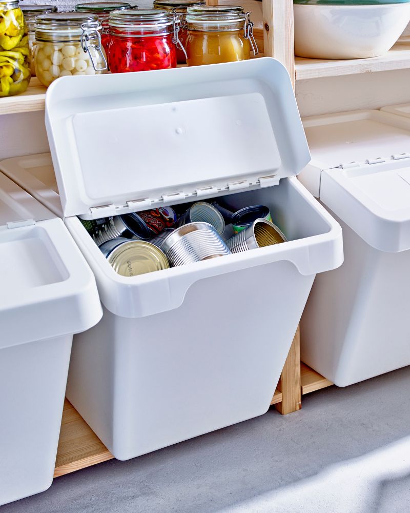 Storage area with SORTERA waste bin, KORKEN jars in multiple sizes, and labeled containers for organizing food and preserves.