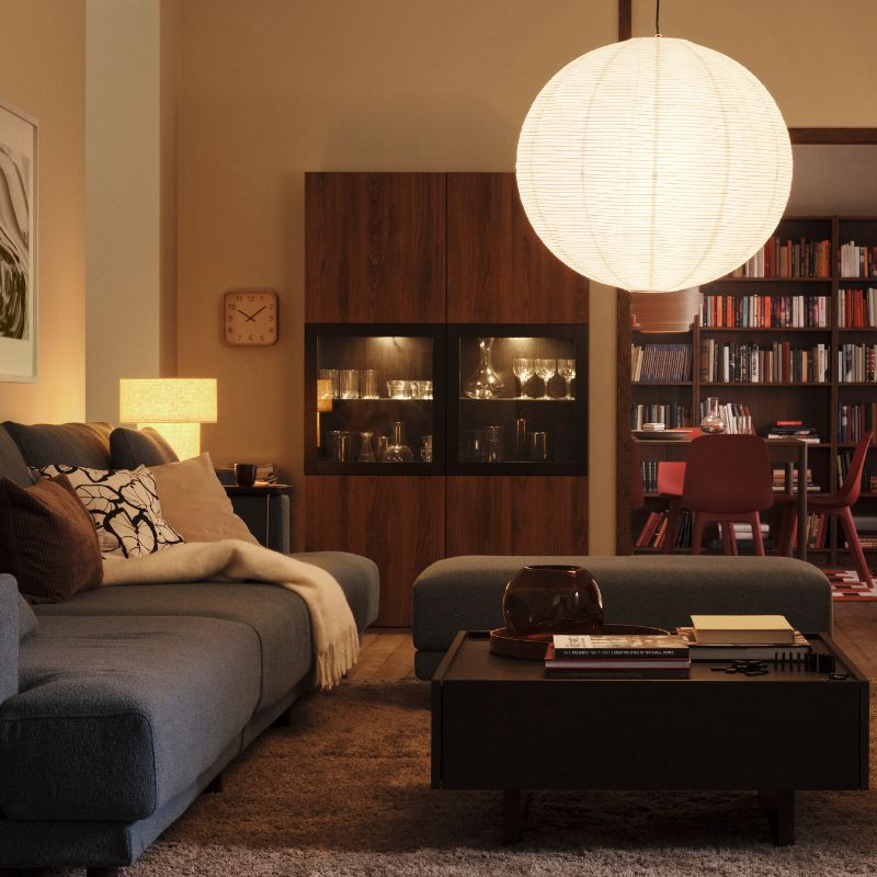A lamp with a GULLSUDARE pendant lampshade hangs in a living room with a STOCKHOLM 2025 table lamp in one corner.