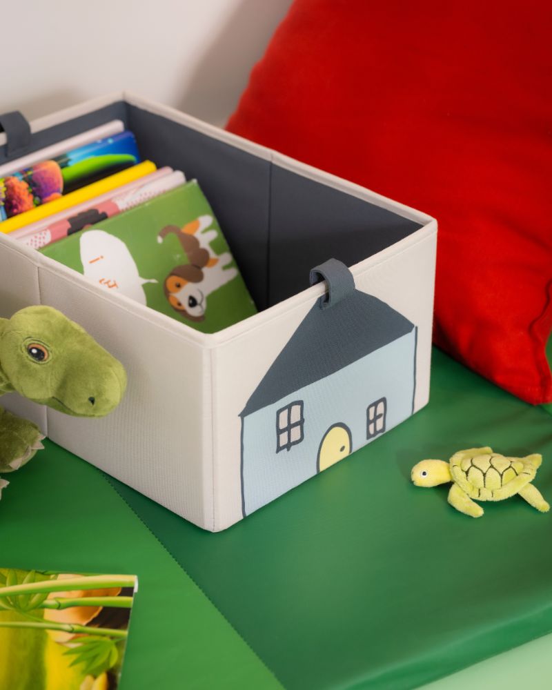 GURLI box with books on a BARNDRÖM mat, next to BLÅVINGAD and PLUFSIG plush toys in a kids’ area.