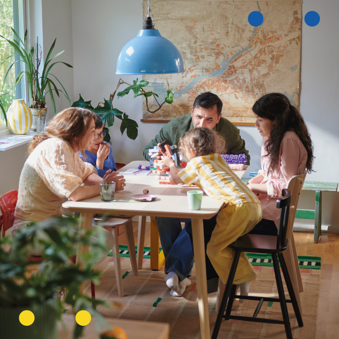 Familia sentada alrededor de una mesa jugando un juego de mesa en un comedor luminoso.