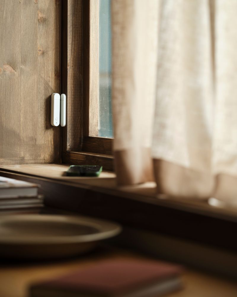 A MYGGBETT door/window sensor is mounted on a window and on the frame of a window. The window is closed.