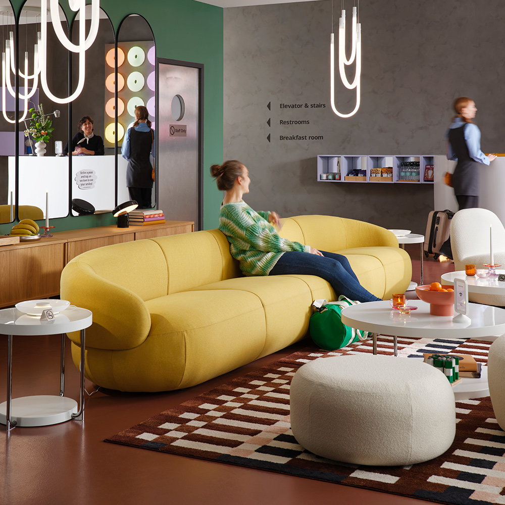 A multicolour/check patterned MARKBLÅMME low pile rug is in modern hotel lounge that has guests on the sofa and at reception.