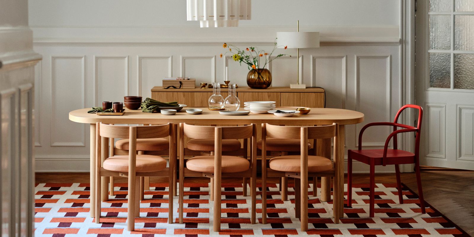 Nordic dining room with warm wood and STOCKHOLM 2025 pieces: table, chairs, tableware, cutlery, vase and lamps.