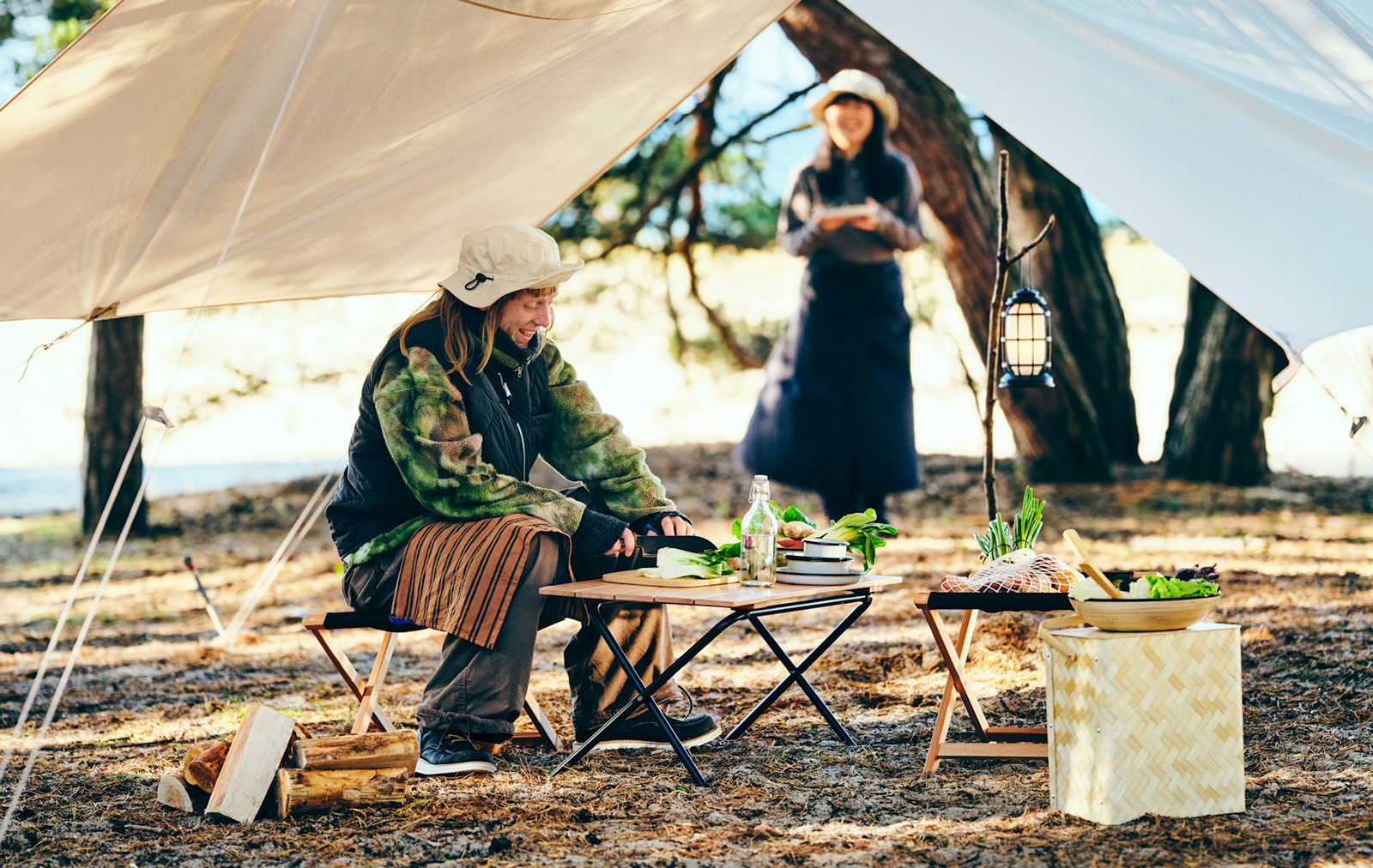 Two smiling people are preparing food with SOLUPPGÅNG collection items in a forest,they are camping