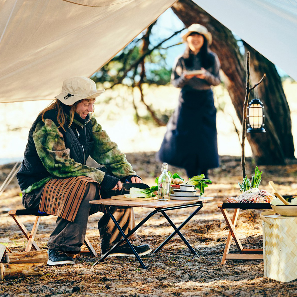 Two smiling people are preparing food with SOLUPPGÅNG collection items in a forest,they are camping
