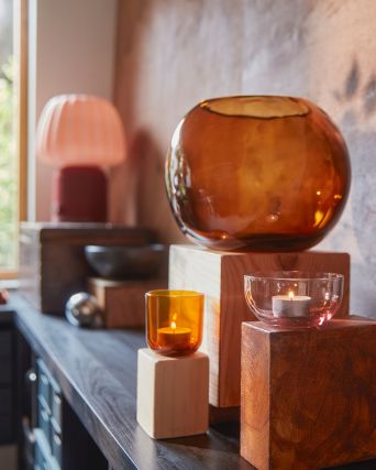 A pink/brown TALLTITA tealight holder set of 2 is placed on some wooden blocks and surrounded by decorative objects.