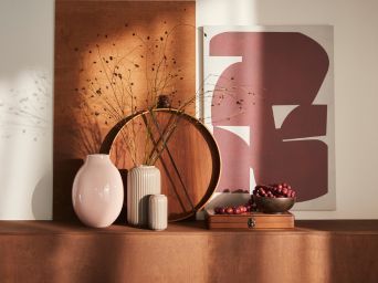 A pale pink BLODBJÖRK vase is placed on a tan surface together with more vases, decorative objects and a PJÄTTERYD picture.