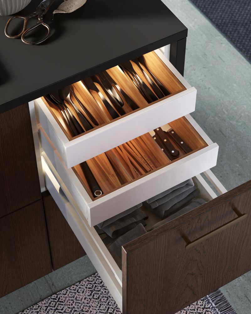 Organized drawer with TILLAGD cutlery, UPPDATERA trays, SNITTA knives and TREBENT chopsticks under the EKBACKEN countertop.