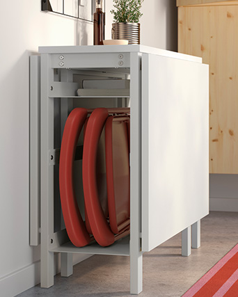 White drop-leaf table with red folding chairs stored inside.