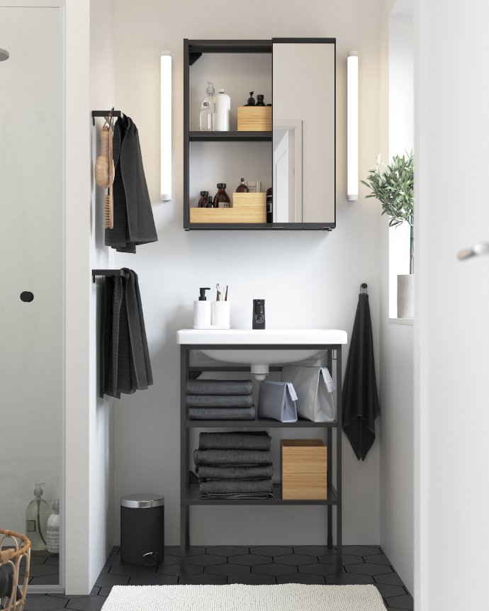 Modern bathroom with a white sink, open vanity with neatly organized towels, a mirrored cabinet with shelves holding bathroom accessories, along with towel racks and a decorative plant.