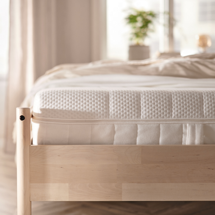 Cama elegante con cabecera tapizada, colchón acolchado y ropa de cama blanca en un dormitorio moderno.