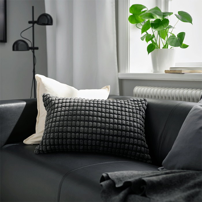 Textured dark grey and white cushions on a black leather sofa in a bright living room.
