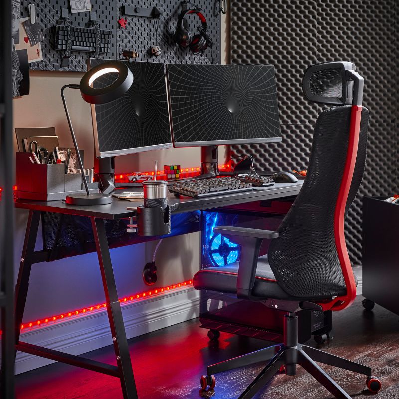 A neon‑lit gaming room with the UTVISNING desk and LÖPARBANA chair, enhanced by the LÅNESPELARE ring light for a vibrant setup.