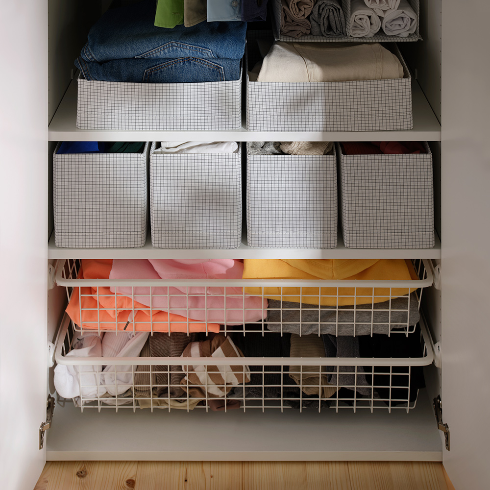 An open wardrobe with folded clothes organised inside STUK boxes with compartments placed on shelves and in wire drawers.