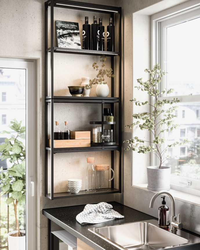 Black metal open shelving in a modern kitchen, holding bottles, spices, tableware, and decorative plants next to a window and sink.