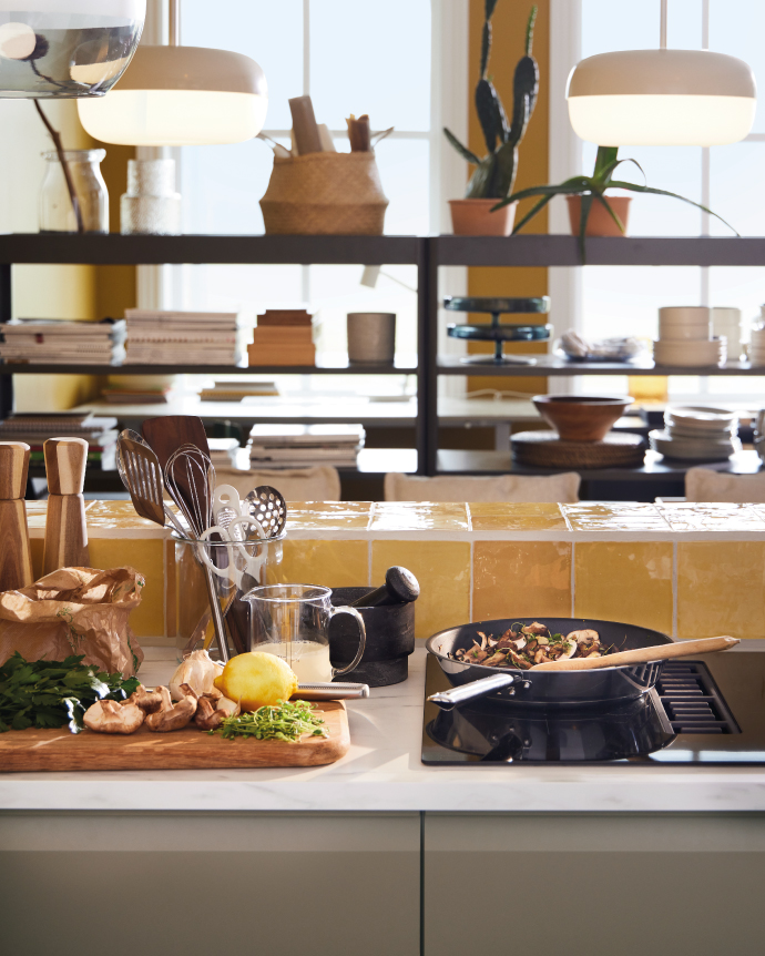 Kitchen countertop with fresh ingredients, a frying pan on the stove, and a bright yellow tile backsplash.