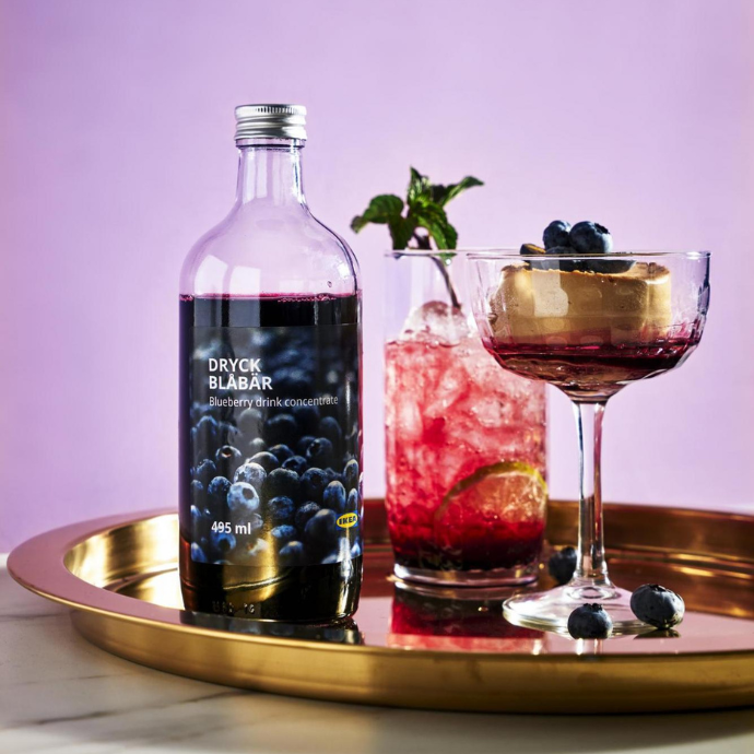 Frozen tea cubes with milkBottle of blueberry drink concentrate next to two iced cocktails with blueberries and mint on a golden tray.