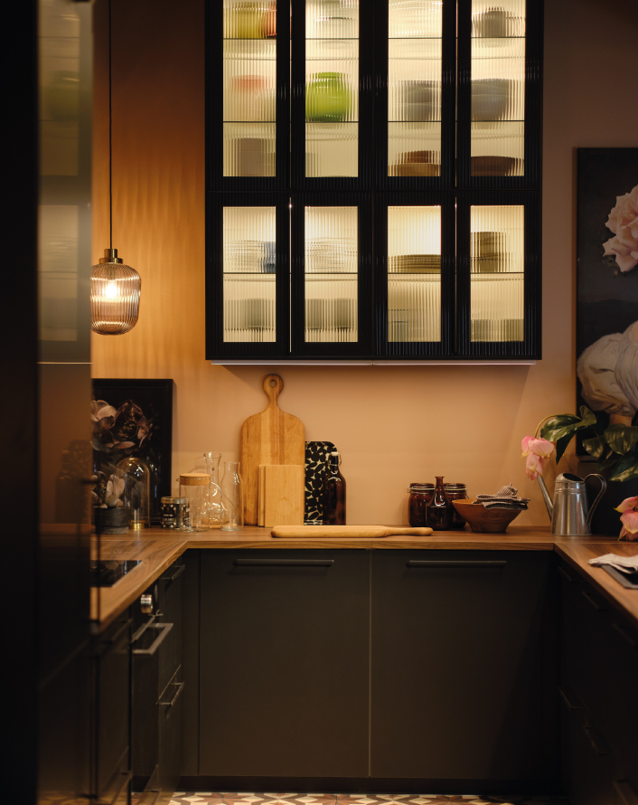 Modern kitchen with warm lighting, glass-front cabinets, and countertop decorated with utensils and jars.