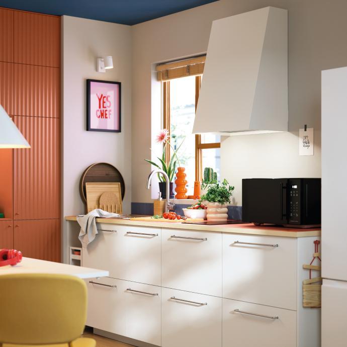 Cocina contemporánea con gabinetes blancos, campana extractora moderna, encimera de madera y decoración colorida cerca de la ventana.