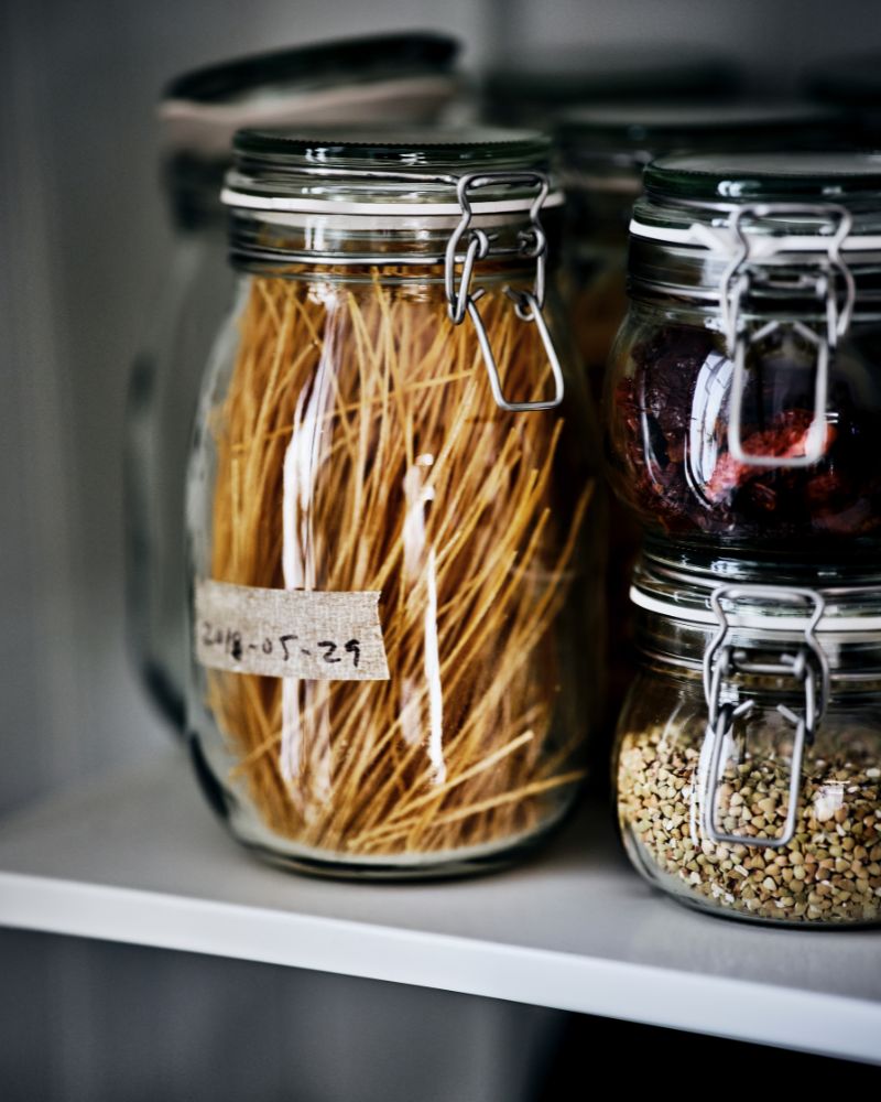 Organized pantry storage with KORKEN jars with lids, glass containers neatly filled with dry foods on open shelving.