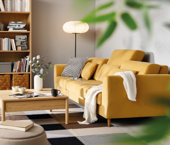 Cama tapizada beige con colchón blanco y ropa de cama estampada junto a una mesita de noche de madera con lámpara y decoración.