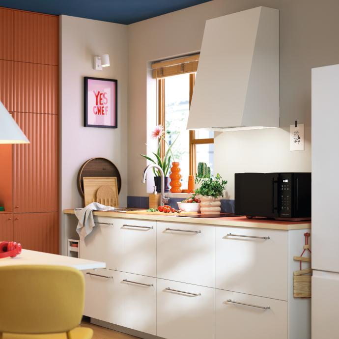 Cocina moderna con detalles coloridos, campana extractora blanca, encimera con vegetales y decoración contemporánea.