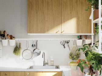 Cocina moderna con gabinetes de madera clara, fregadero bajo repisas abiertas y utensilios colgados en pared blanca.