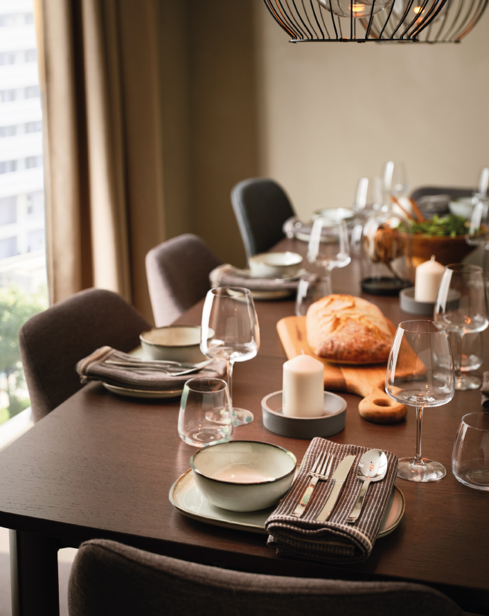 Elegant dining table set with plates, wine glasses, candles, and a loaf of bread on a wooden table by a window.