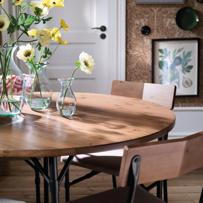 Close-up of a round wooden dining table with black metal legs and yellow flowers in glass vases.
