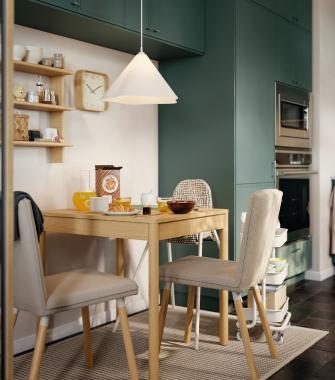 A light wood dining table set for four with pink plates, red cushions, and two terracotta pendant lamps.