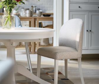 Detail of a long butcher-block style wooden table with white bowls and black spindle chairs in the background.