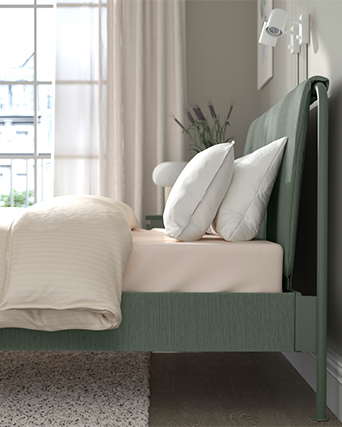 Primer plano de un colchón grueso de color beige con asa lateral, apoyado sobre una estructura de cama de madera blanca minimalista.